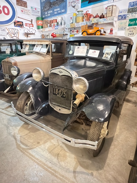 Restored vintage cars displayed in a museum, showcasing a black 1920s model with a classic front grille and authentic license plate.