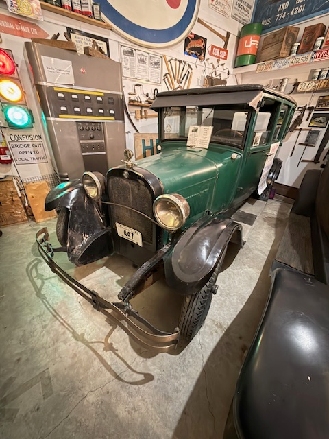 A vintage green 1920s car displayed in a museum filled with historical signs and artifacts, showcasing automotive history.